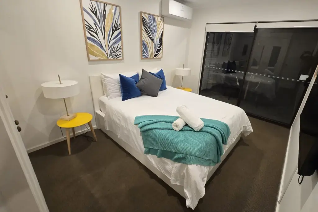 The same bedroom photographed on a phone, with a reflection in the glass doors