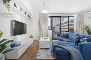 Living room with a blue sectional sofa, wall-mounted TV and balcony doors in an East Perth apartment