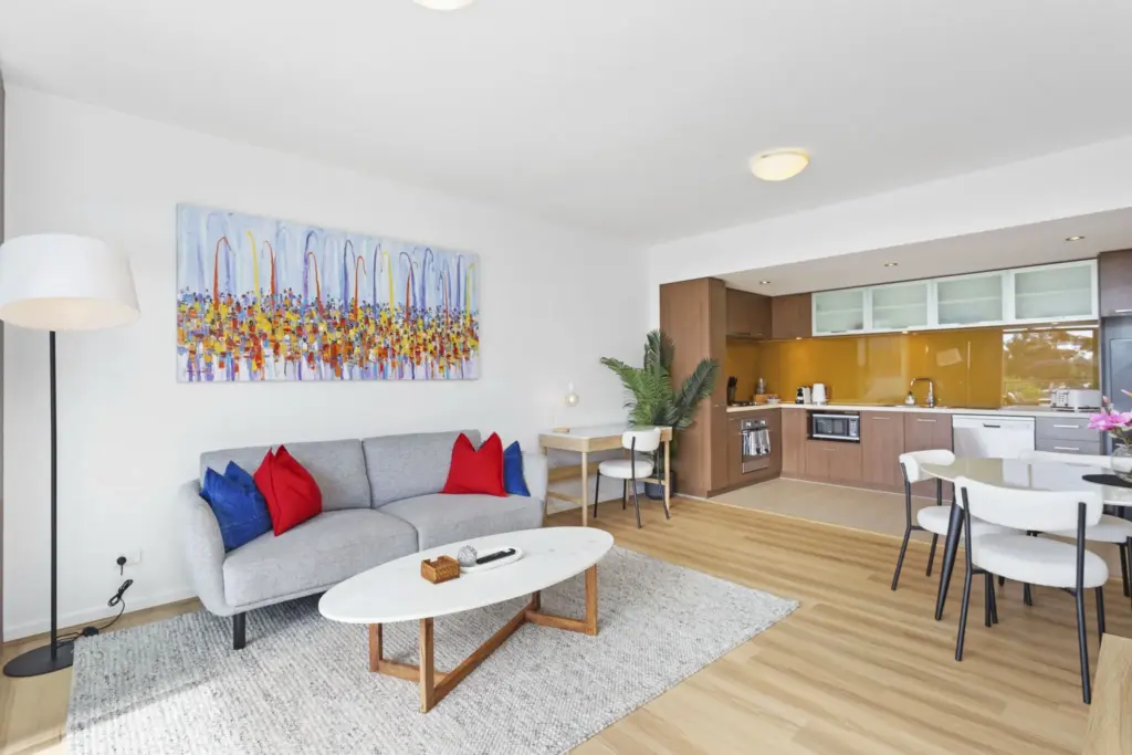 Open-plan living area with a grey sofa, colourful artwork and a timber kitchen in a Perth apartment